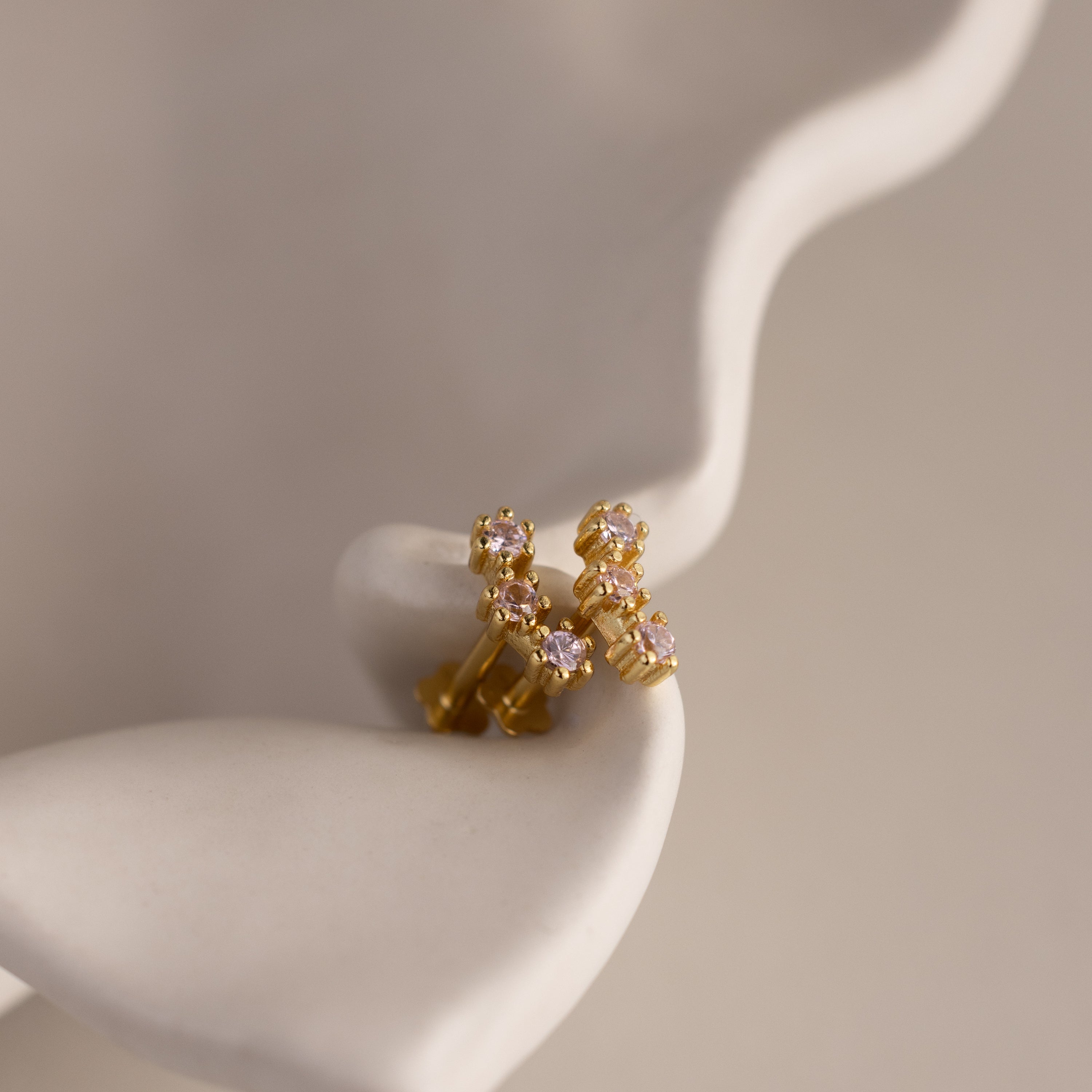 Ruby Cluster Flatback Studs featuring small, colorful gemstones are displayed on a curved, white abstract surface.