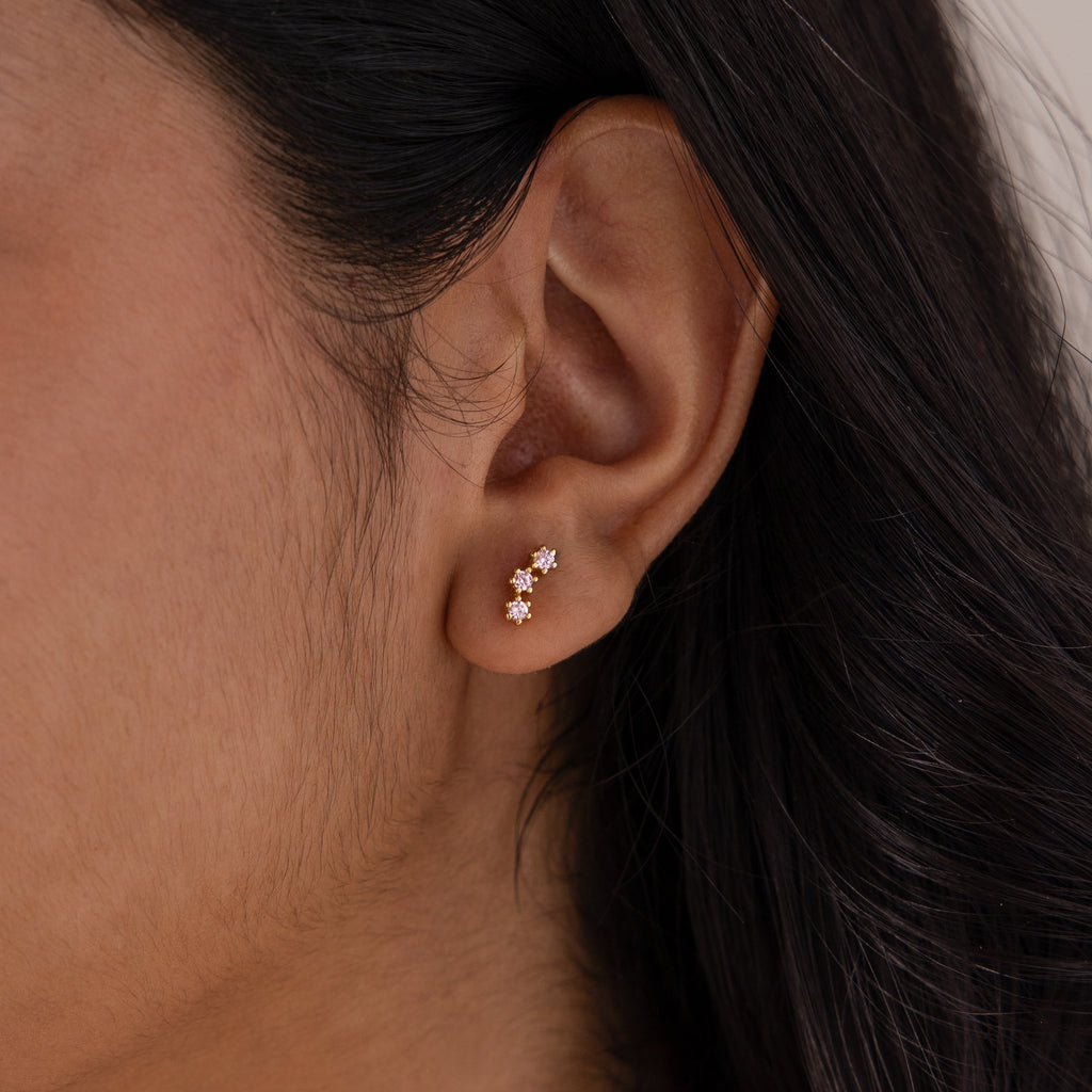 Close-up of an ear wearing two gold flower-shaped stud earrings with pink stones, ideal for pairing with Birthstone Cluster Flatback Studs.