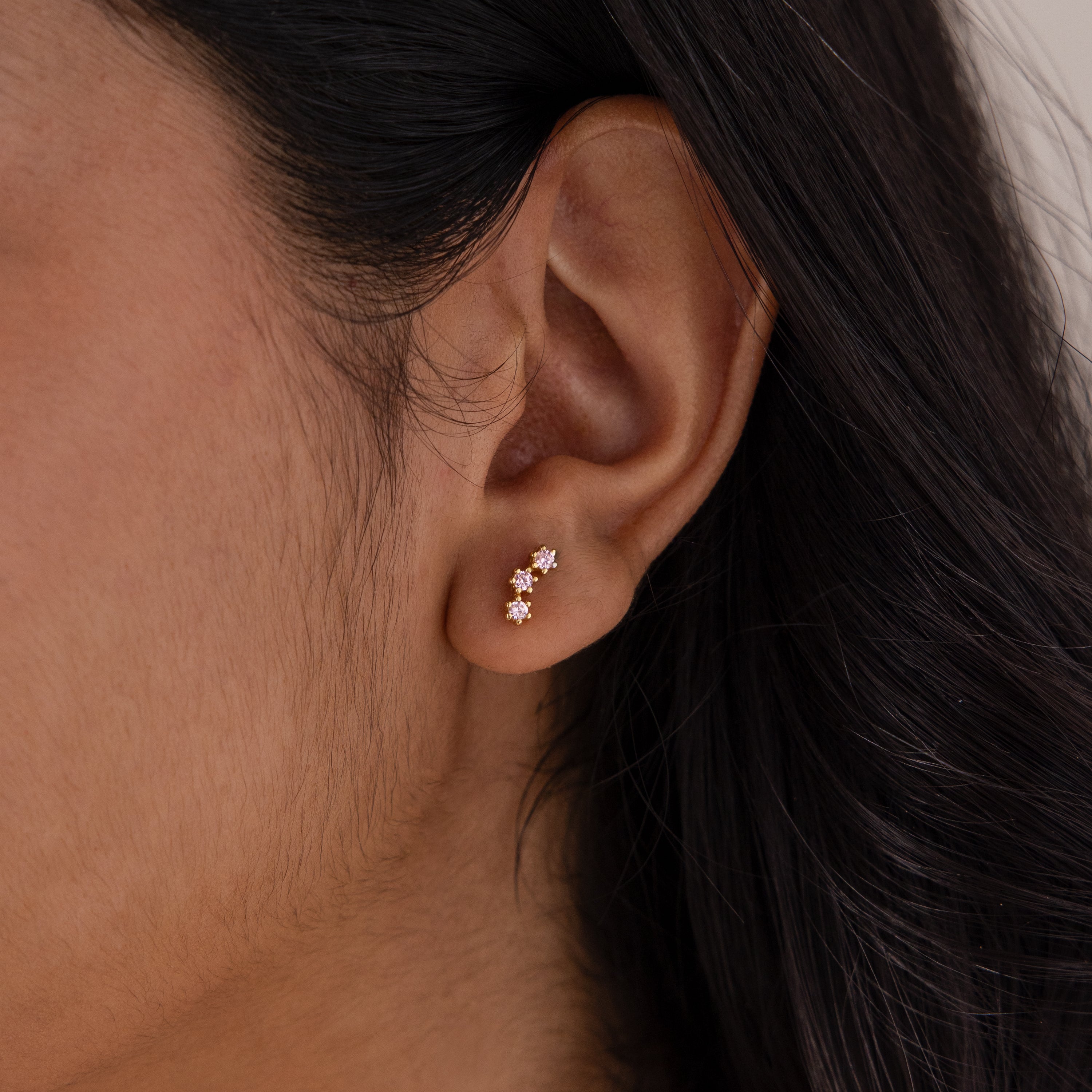 Close-up of an ear wearing two gold flower-shaped stud earrings with pink stones, ideal for pairing with Birthstone Cluster Flatback Studs.