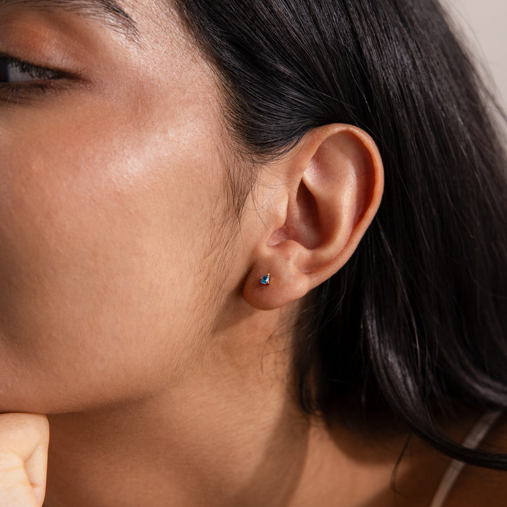 Close-up of a woman's ear wearing Teardrop Blue Zircon Flatback Studs; her hand rests under her chin.