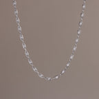 Close-up of a delicate silver chain necklace with oval pearl links, suspended against a neutral backdrop.