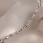 Close up of a silver pearl chain necklace with small white pearls set in oval gold links, displayed on a soft neutral fabric background.