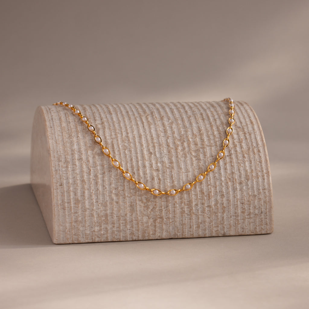 Pearl chain necklace draped over a textured display stand, softly lit in a warm, minimal setting.