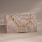 Pearl chain necklace draped over a textured display stand, softly lit in a warm, minimal setting.