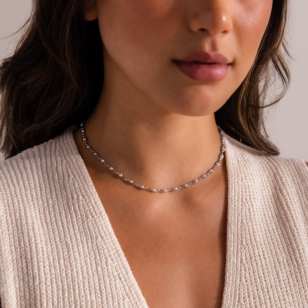 Silver choker necklace featuring evenly spaced white pearls, styled on a woman’s neckline with a textured cream knit top.