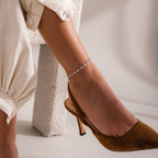 Close-up of a silver chain bracelet with white pearls set in oval links, displayed against a soft neutral fabric background.