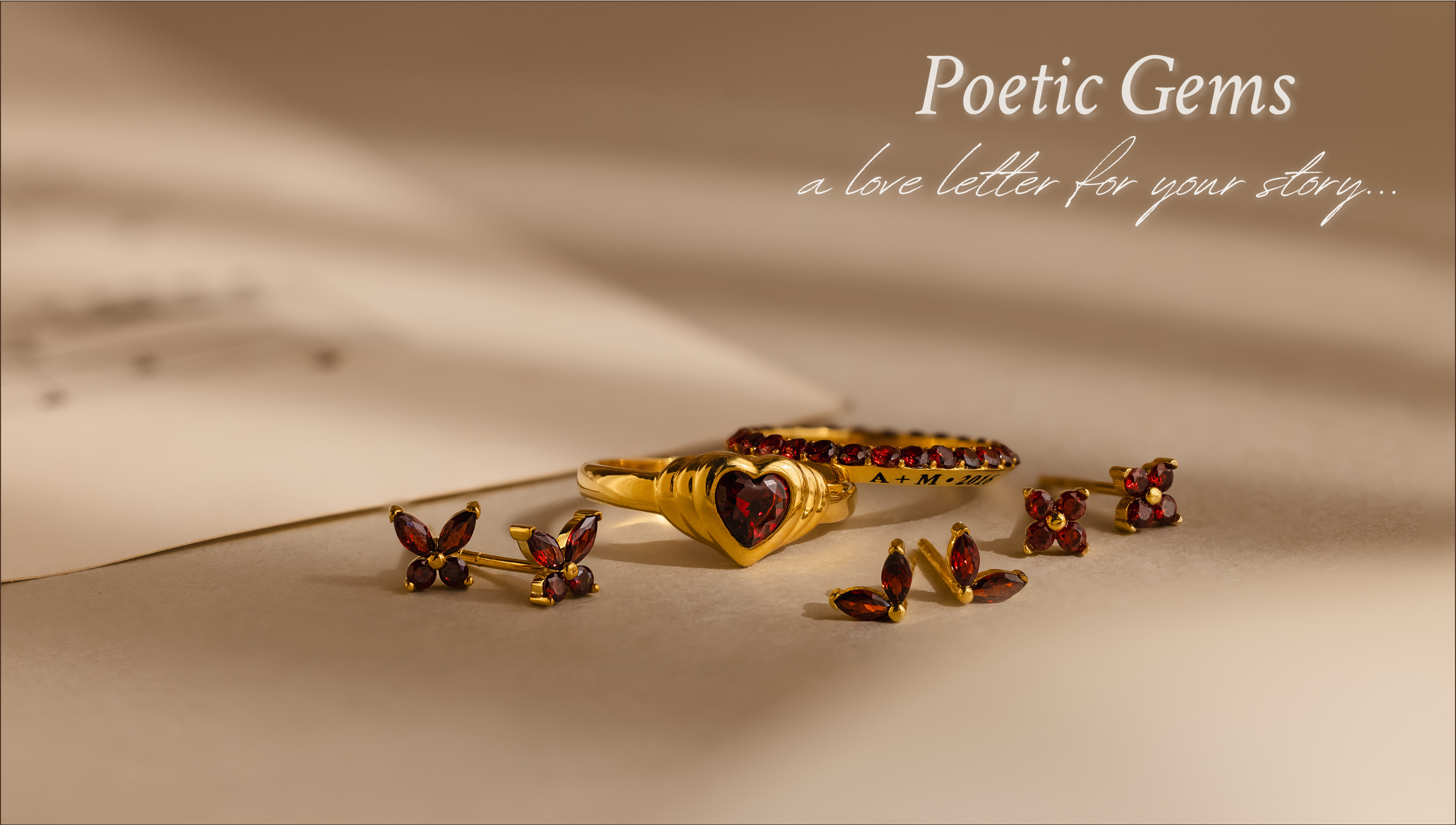 A landscape jewelry flat lay with the text "Poetic gems a love letter for your story" featuring custom birthstone items: butterfly studs, heart signet ring, engravable eternity ring, ivy flower studs, and marquise petal studs - all in the color January Red Garnet.