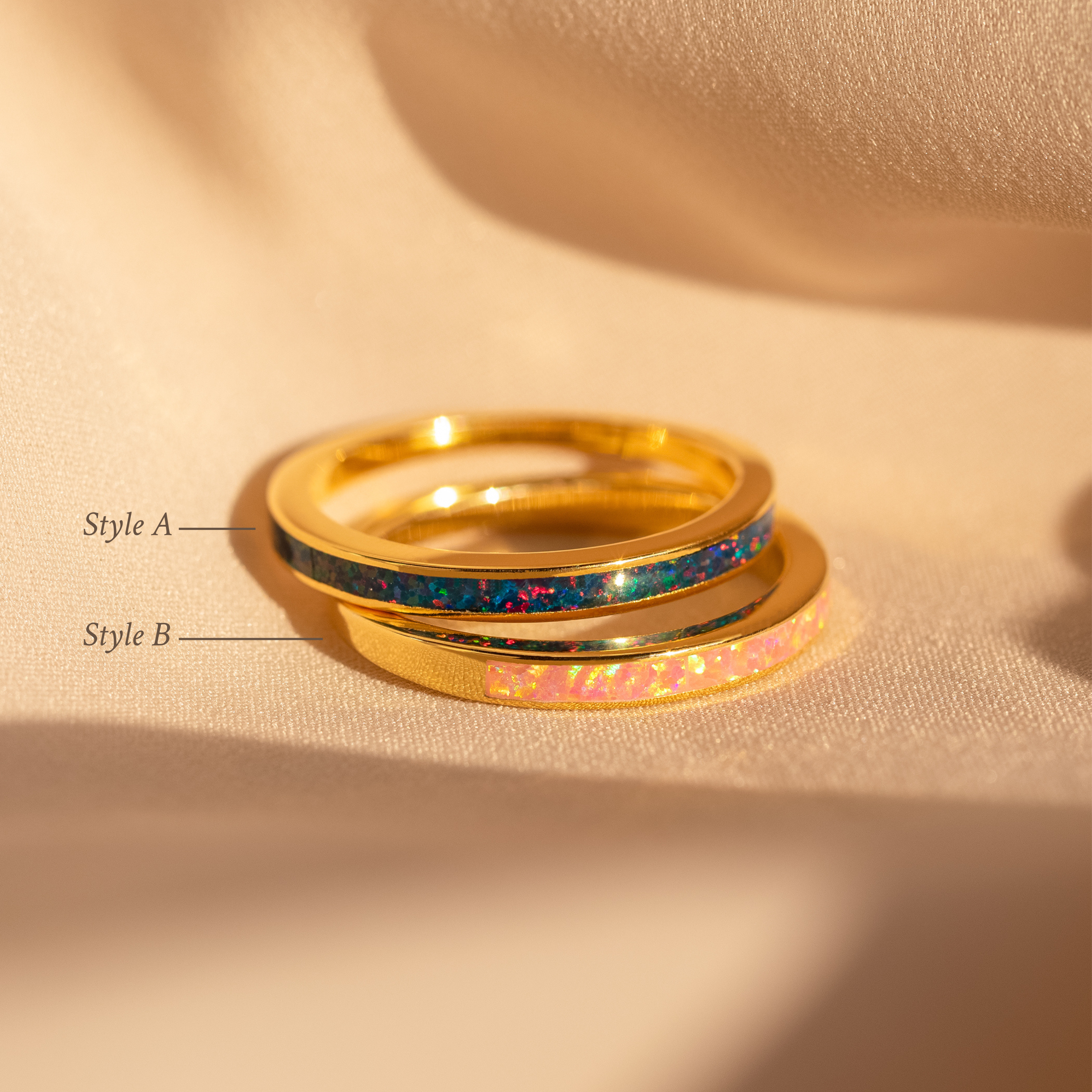 The Opal Inlay Rings Set rests on beige fabric: one ring features an indigo blue inlay, while the other showcases a Pink Flamingo inlay.