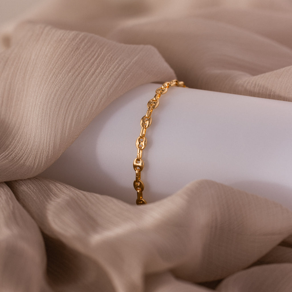 Mini Mariner Chain Bracelet in gold, draped over soft beige fabric.