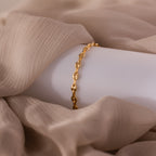 Mini Mariner Chain Bracelet in gold, draped over soft beige fabric.