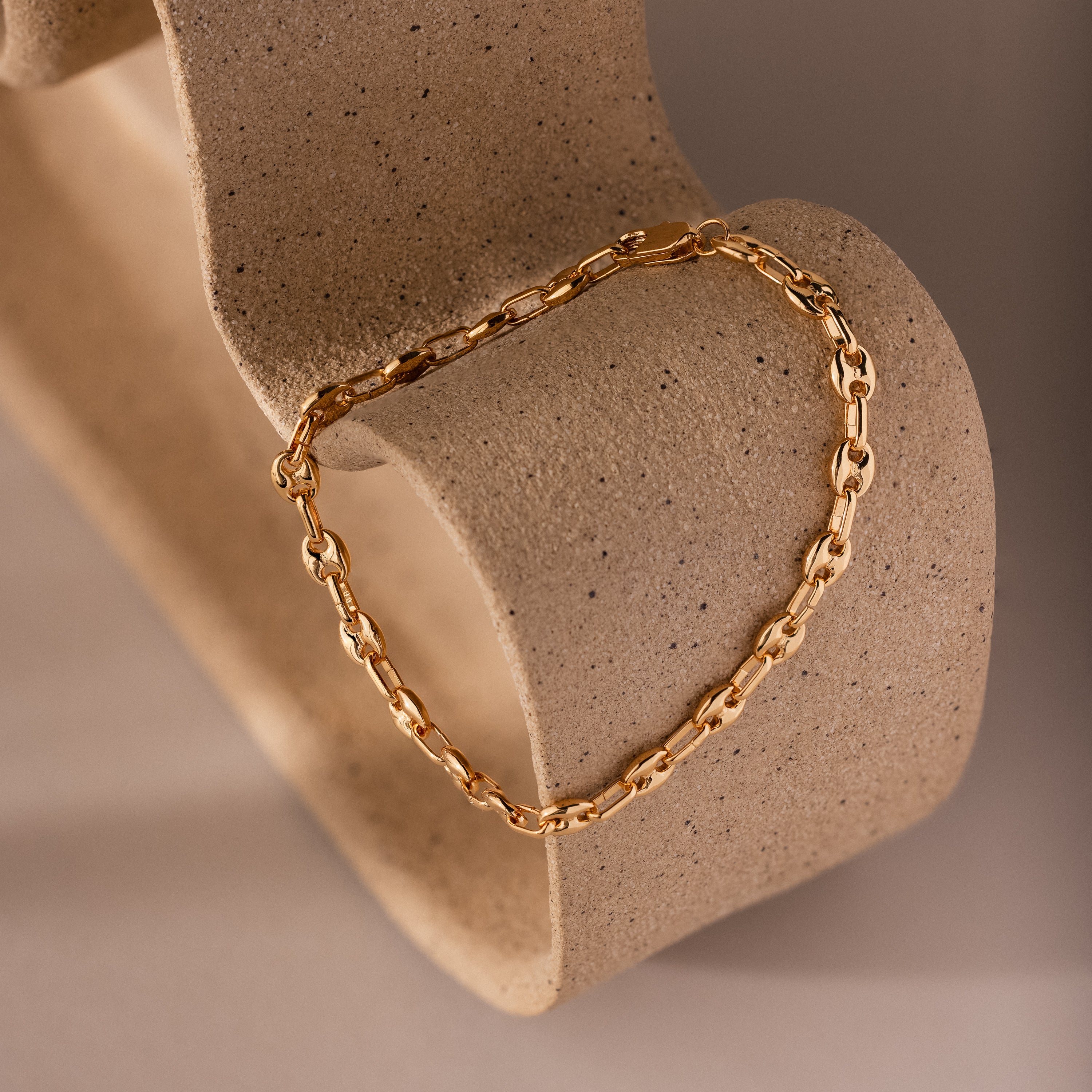 Mini Mariner Chain Bracelet displayed on a sculptural stone form, showcasing its delicate gold links and polished finish.
