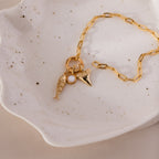 Gold chain bracelet with three ocean-inspired charms: a textured fish, a round white accent, and a shark tooth pendant.