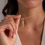 Gold Fish Charm placed on delicate chain necklace, being held up close, styled on neckline with a soft knit top.