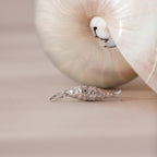 Silver fish charm with detailed scale texture, styled beside a pearlescent seashell.