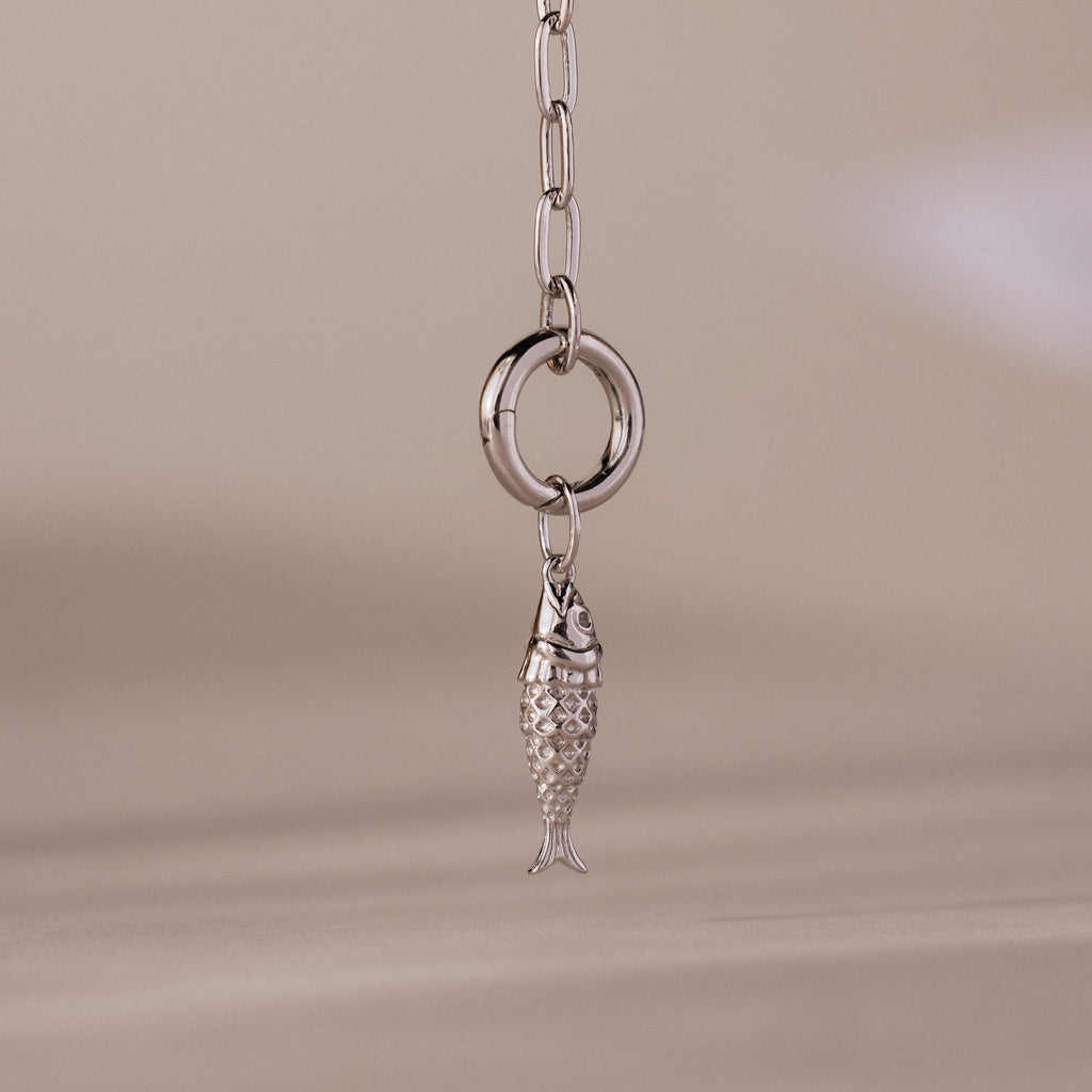 Silver fish charm pendant with intricate scale detailing, hanging from a polished circular link on a chain.