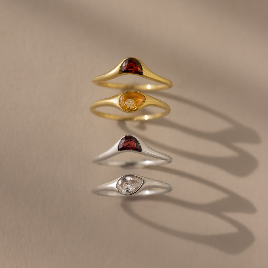 The Sculpted Toi et Moi Ring Set features four gold and silver rings with teardrop-shaped stones, ideal for stacking or making a statement. Their delicate design casts soft shadows on beige, enhancing any look.