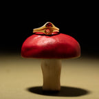 A Sculpted Toi et Moi Ring set in 18K Gold, featuring two red gemstones, rests atop a red and white mushroom under dramatic lighting.