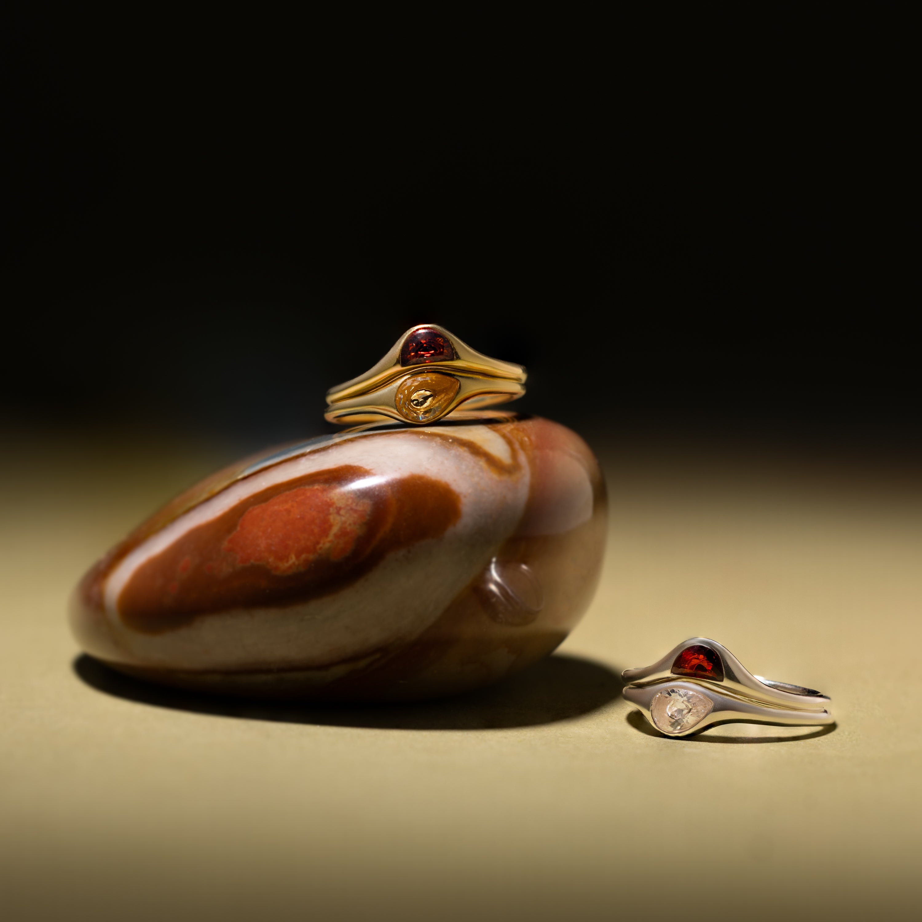 The Sculpted Toi et Moi Ring Set in Silver is displayed on and beside a polished brown stone against a plain background.