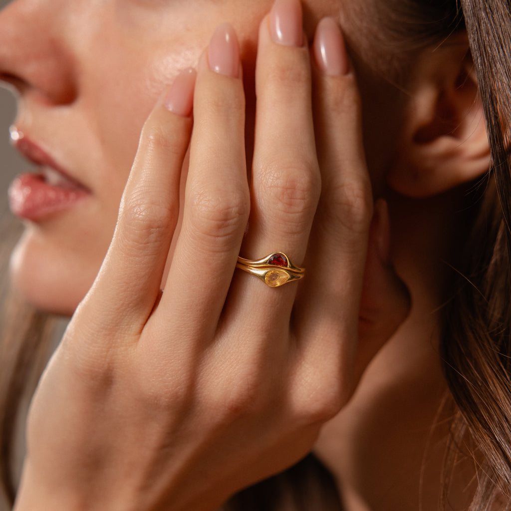 A woman’s hand rests near her face, adorned with the Sculpted Toi et Moi Ring Set in 18K Gold featuring red and yellow stones. Her nails are painted with nude polish.