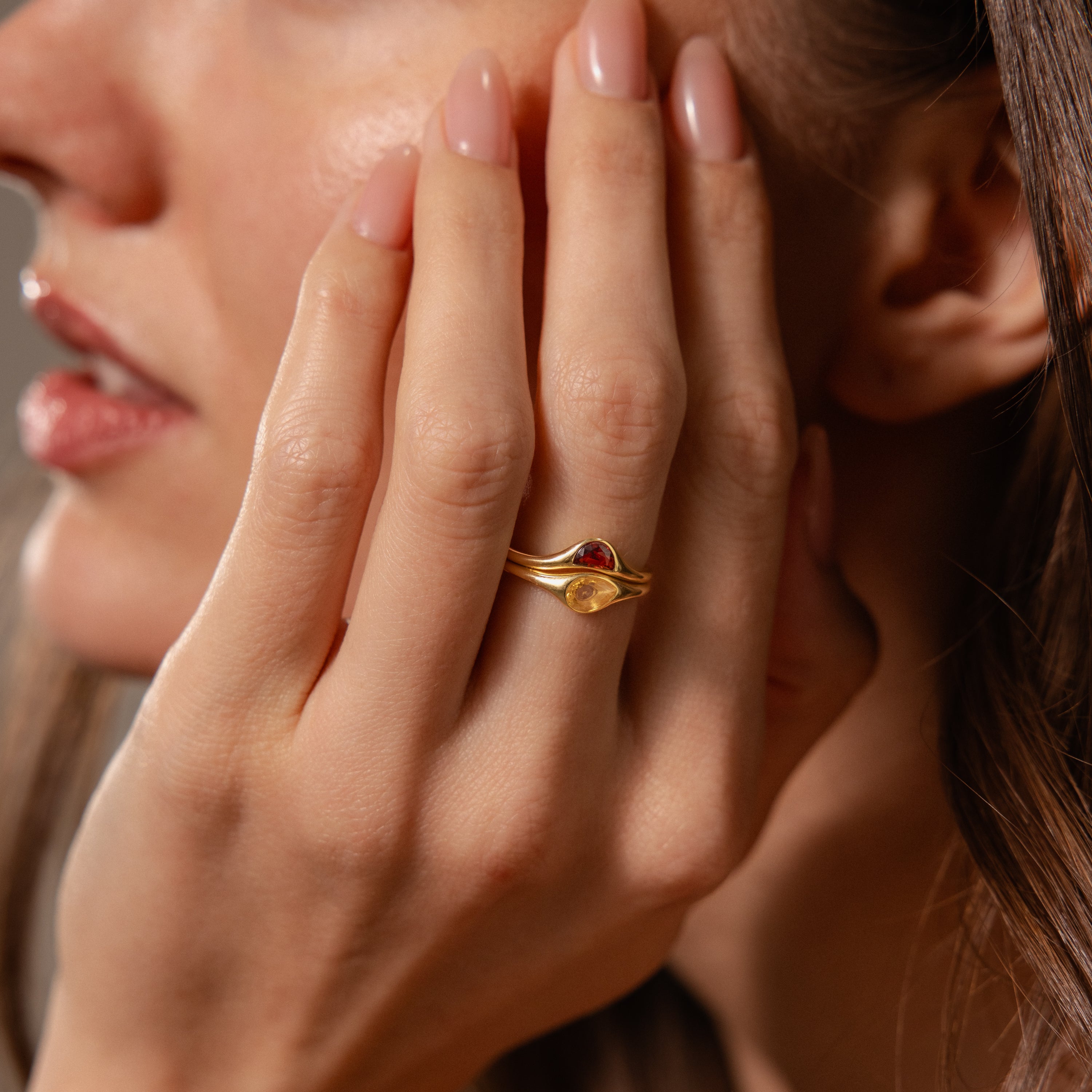 A woman with manicured nails touches her face, wearing the Sculpted Toi et Moi Ring Set and a dazzling gold gemstone ring on her ring finger.