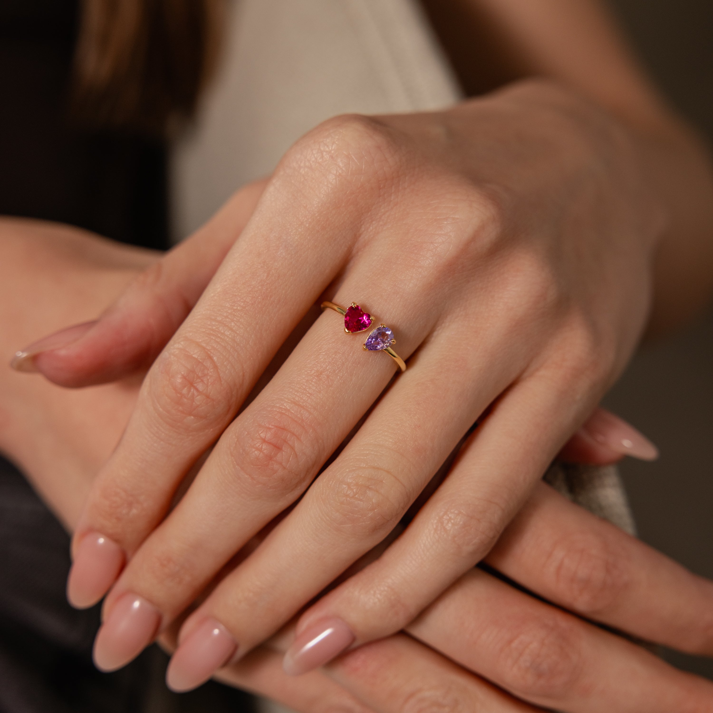 A hand with manicured nails wears the Love Toi et Moi Ring, a gold stacking ring set with red and purple gemstones for a chic look.