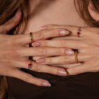Close-up of hands with nude manicured nails wearing gold rings, including the Love Toi et Moi Ring, resting on a brown fabric top.