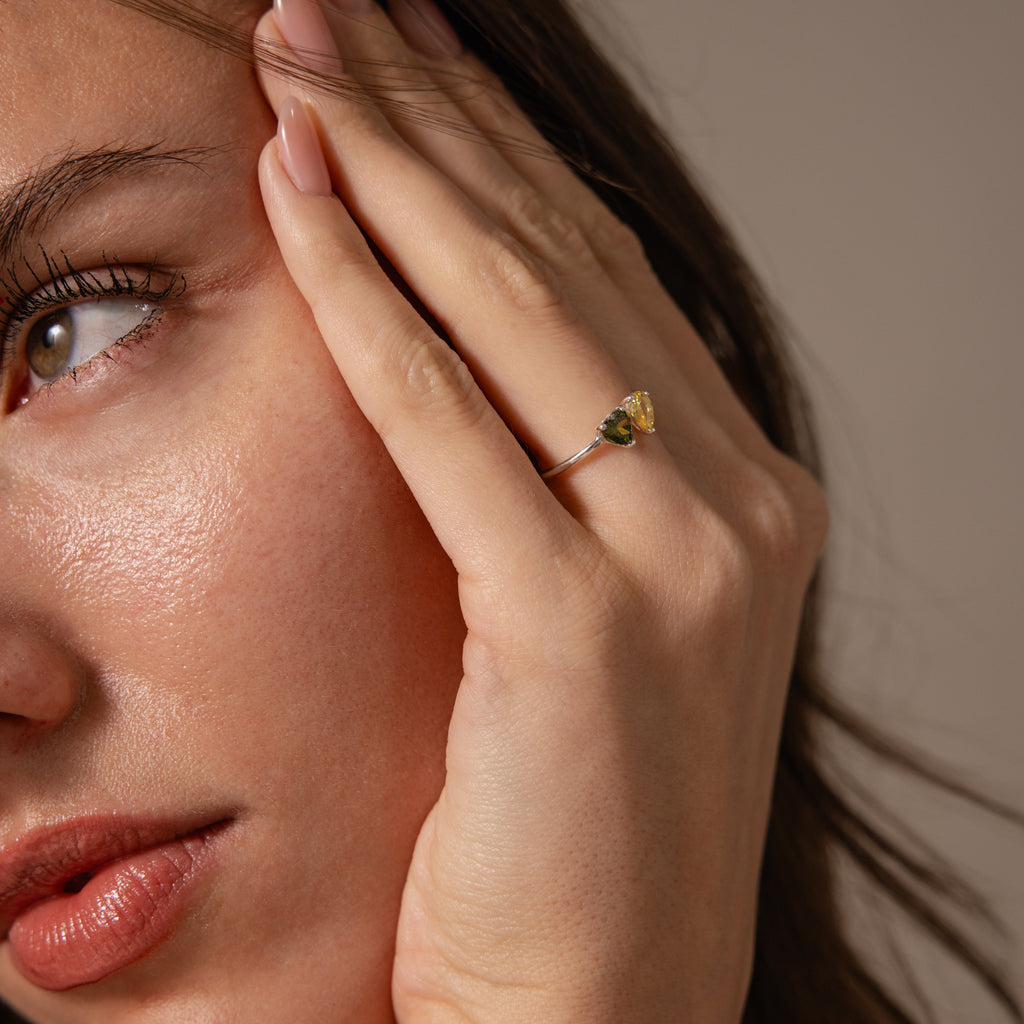 A woman touches her face while wearing the Love Toi et Moi Ring in Silver, featuring a striking yellow gemstone on her finger.