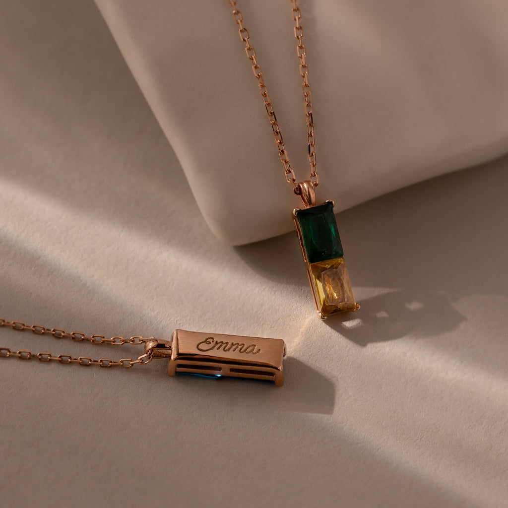The Duo Birthstone Name Necklace in Rose Gold features two stylish pendants: one with green and yellow birthstones, and another as a custom-engraved bar reading "Emma"—a stunning piece of personalized jewelry.