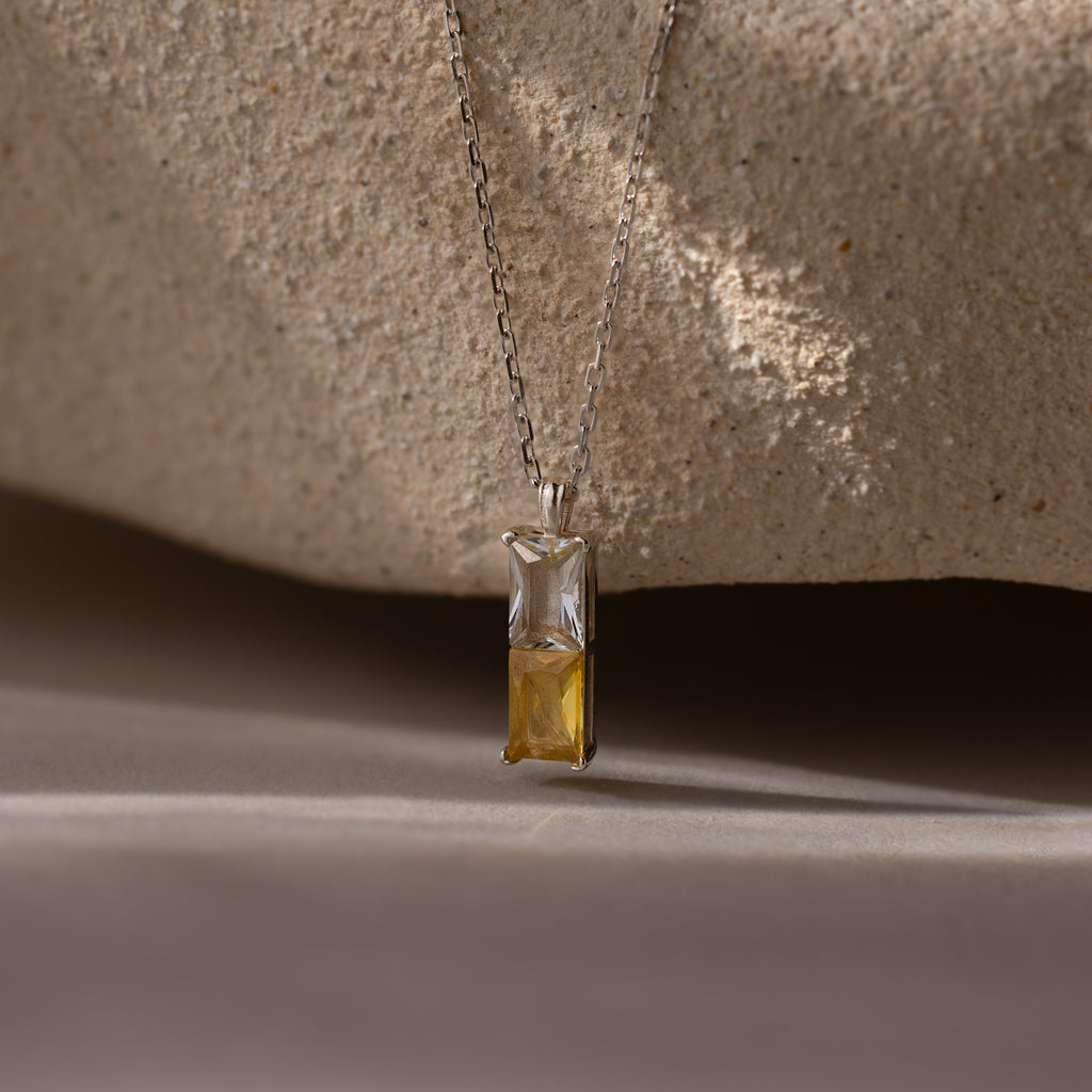 The Duo Birthstone Name Necklace in Sterling Silver features a pendant with one clear and one yellow rectangular gemstone, ideal as personalized jewelry or a unique birthstone name necklace, displayed on a neutral background.