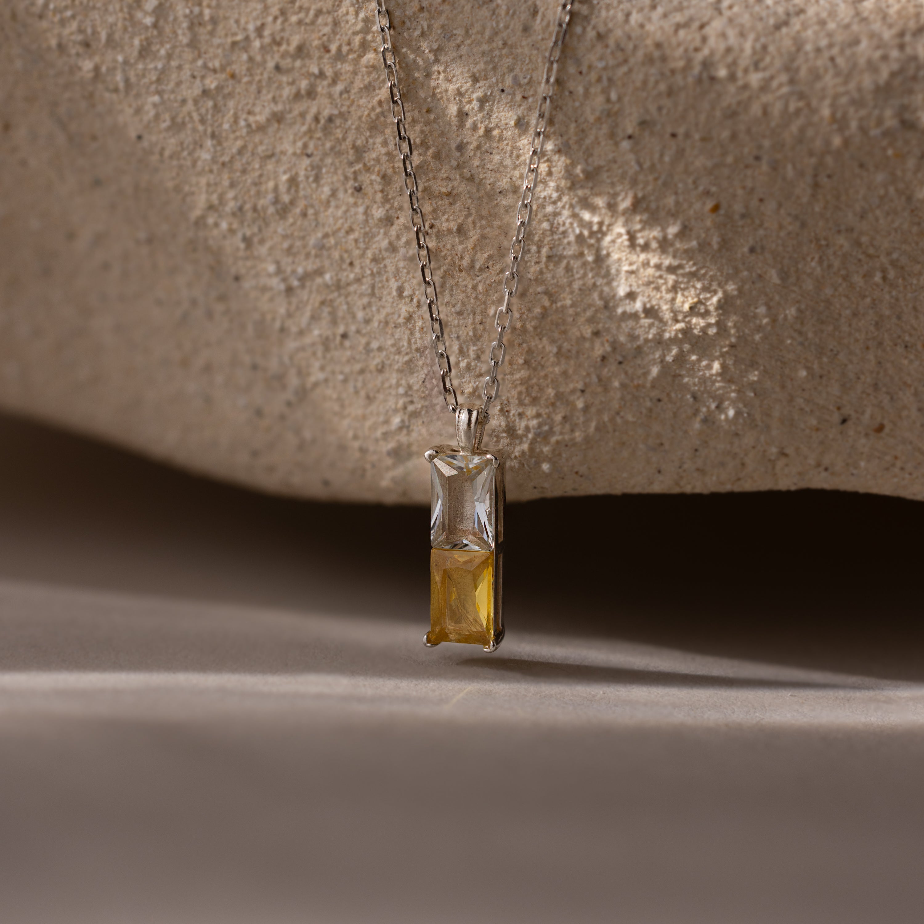The Duo Birthstone Name Necklace in Sterling Silver features a pendant with one clear and one yellow rectangular gemstone, ideal as personalized jewelry or a unique birthstone name necklace, displayed on a neutral background.