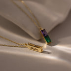 The Duo Birthstone Name Necklace in 18K Gold features two gold pendants on chains, each with rectangular green and purple gemstones—one personalized with the name Skylar for a unique keepsake.