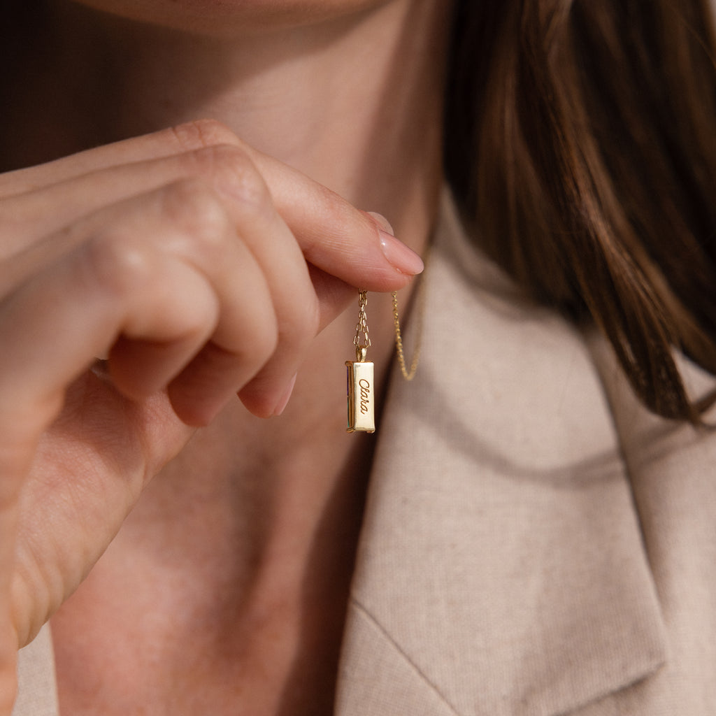 A woman holds the Duo Birthstone Name Necklace in Rose Gold, adorned with a personalized rectangular pendant, highlighting the unique elegance of customized jewelry.