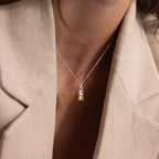 A woman wears a beige blazer and the Duo Birthstone Name Necklace in Sterling Silver, featuring a rectangular yellow gemstone pendant for a personalized touch.