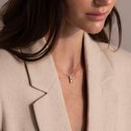 Woman in a beige blazer wears the Duo Birthstone Name Necklace—a silver chain featuring a yellow rectangular pendant, personalized with elegant custom name engraving for a unique keepsake style.