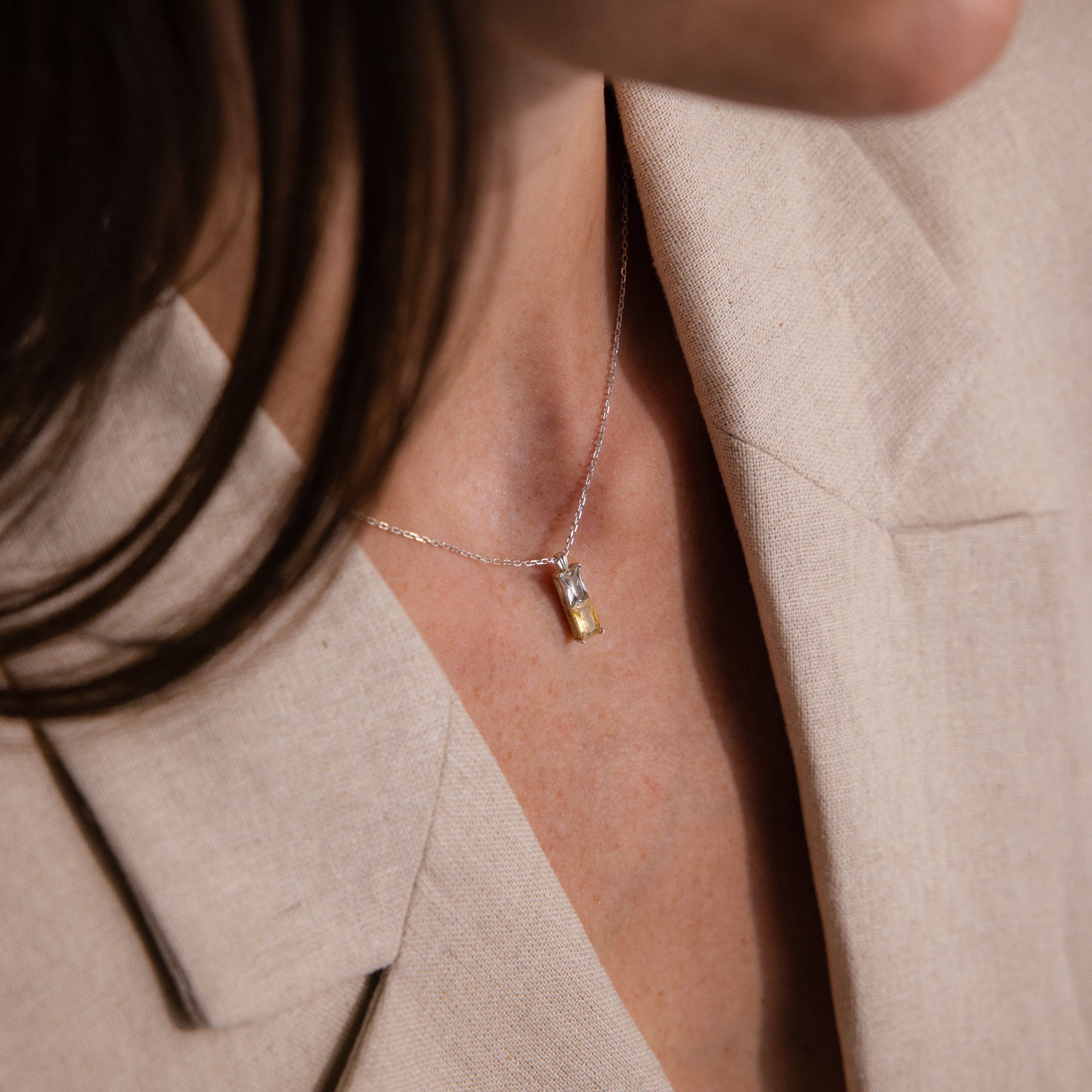 Close-up of a person wearing a beige blazer and the Duo Birthstone Name Necklace in Sterling Silver, featuring a personalized rectangular pendant.