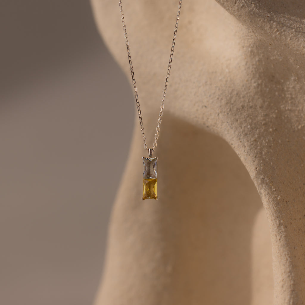 Duo Birthstone Name Necklace in Sterling Silver—features a rectangular gemstone on a smooth beige surface; a stunning piece of personalized jewelry, ideal for custom name engraving or as a unique birthstone necklace.