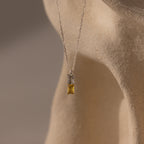 Duo Birthstone Name Necklace in Sterling Silver—features a rectangular gemstone on a smooth beige surface; a stunning piece of personalized jewelry, ideal for custom name engraving or as a unique birthstone necklace.