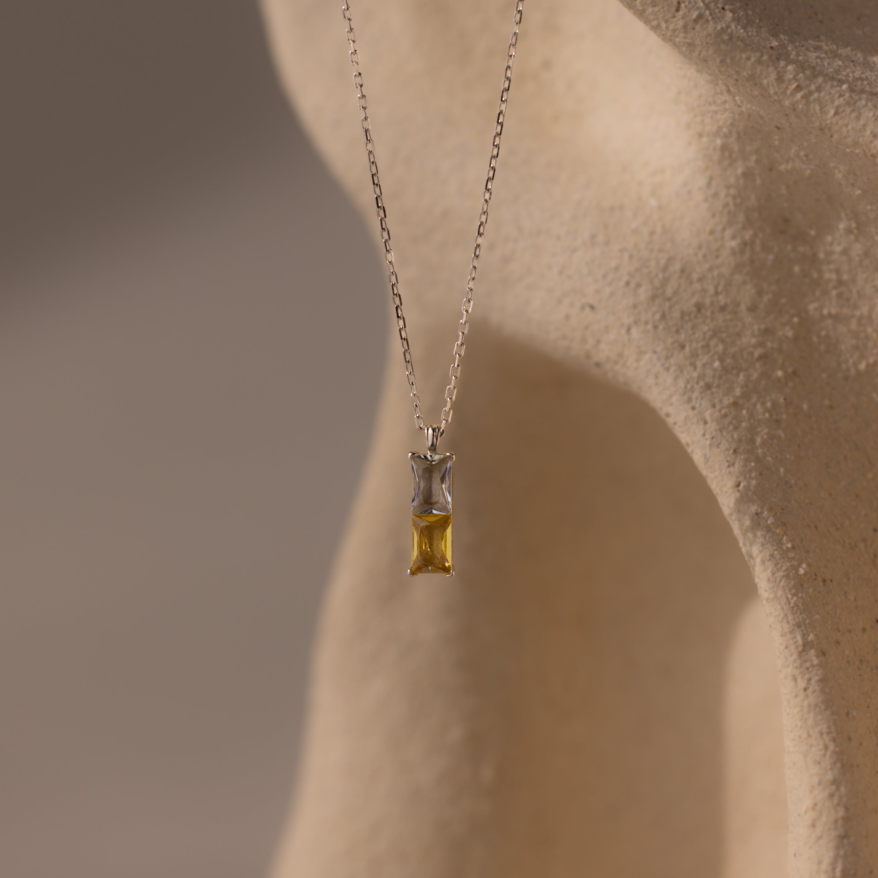 Duo Birthstone Name Necklace in Sterling Silver—features a rectangular gemstone on a smooth beige surface; a stunning piece of personalized jewelry, ideal for custom name engraving or as a unique birthstone necklace.