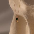 Duo Birthstone Name Necklace in Rose Gold with green and yellow rectangular stones, displayed on a beige textured mannequin. Personalize this unique piece for a one-of-a-kind birthstone name jewelry look.