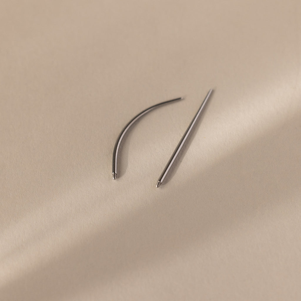 A Flatback Applicator Tool, featuring one curved and one straight needle, rests on a beige surface with soft shadows.