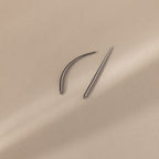 A Flatback Applicator Tool, featuring one curved and one straight needle, rests on a beige surface with soft shadows.