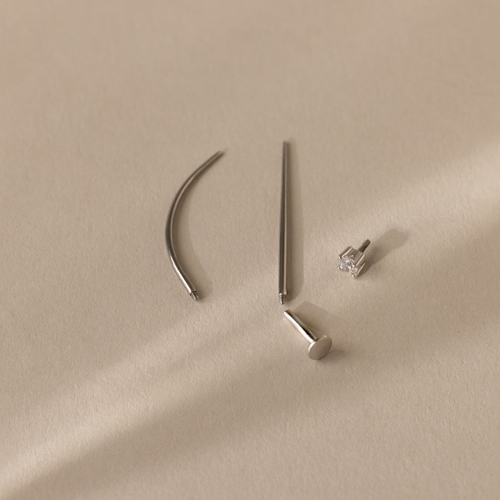 The Flatback Applicator Tool is displayed on a light beige surface alongside four minimalist silver earrings, one featuring a gemstone stud.