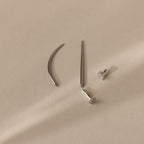 The Flatback Applicator Tool is displayed on a light beige surface alongside four minimalist silver earrings, one featuring a gemstone stud.