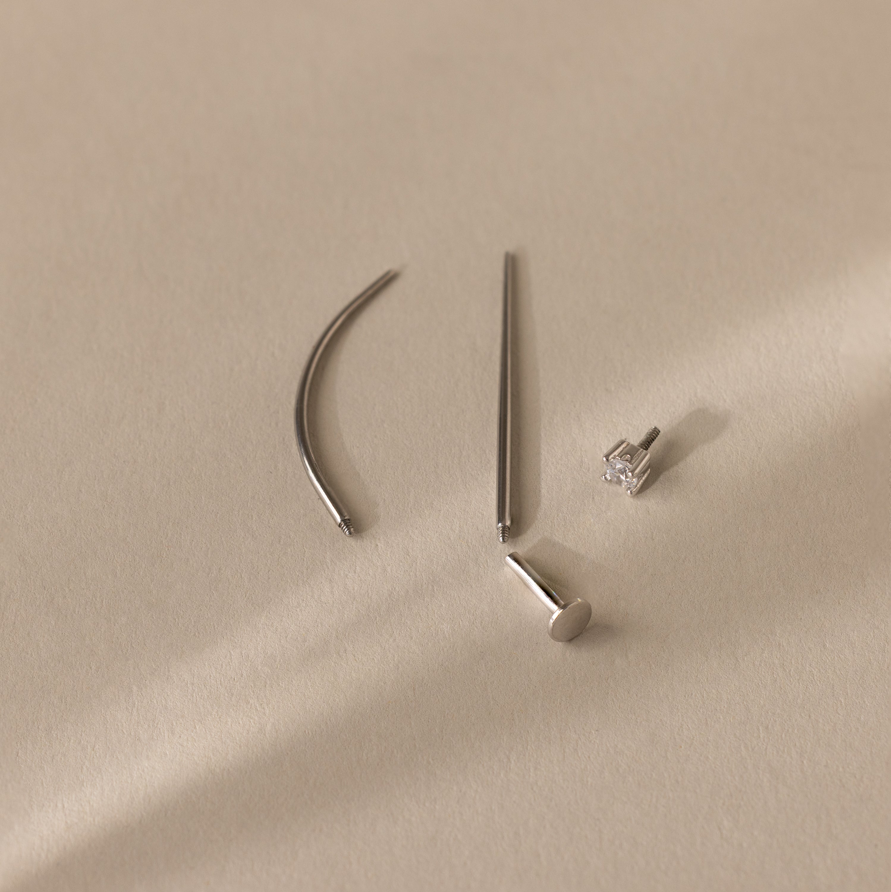 The Flatback Applicator Tool is displayed on a light beige surface alongside four minimalist silver earrings, one featuring a gemstone stud.