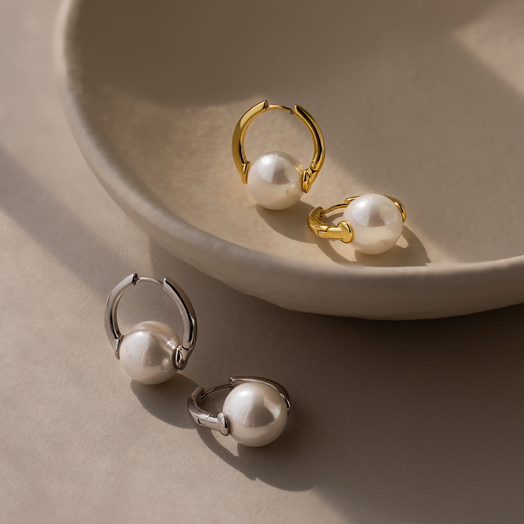 The Bold Round Pearl Hoops in Silver are displayed on a beige ceramic dish, highlighting modern jewelry with bold earrings perfect for any occasion.