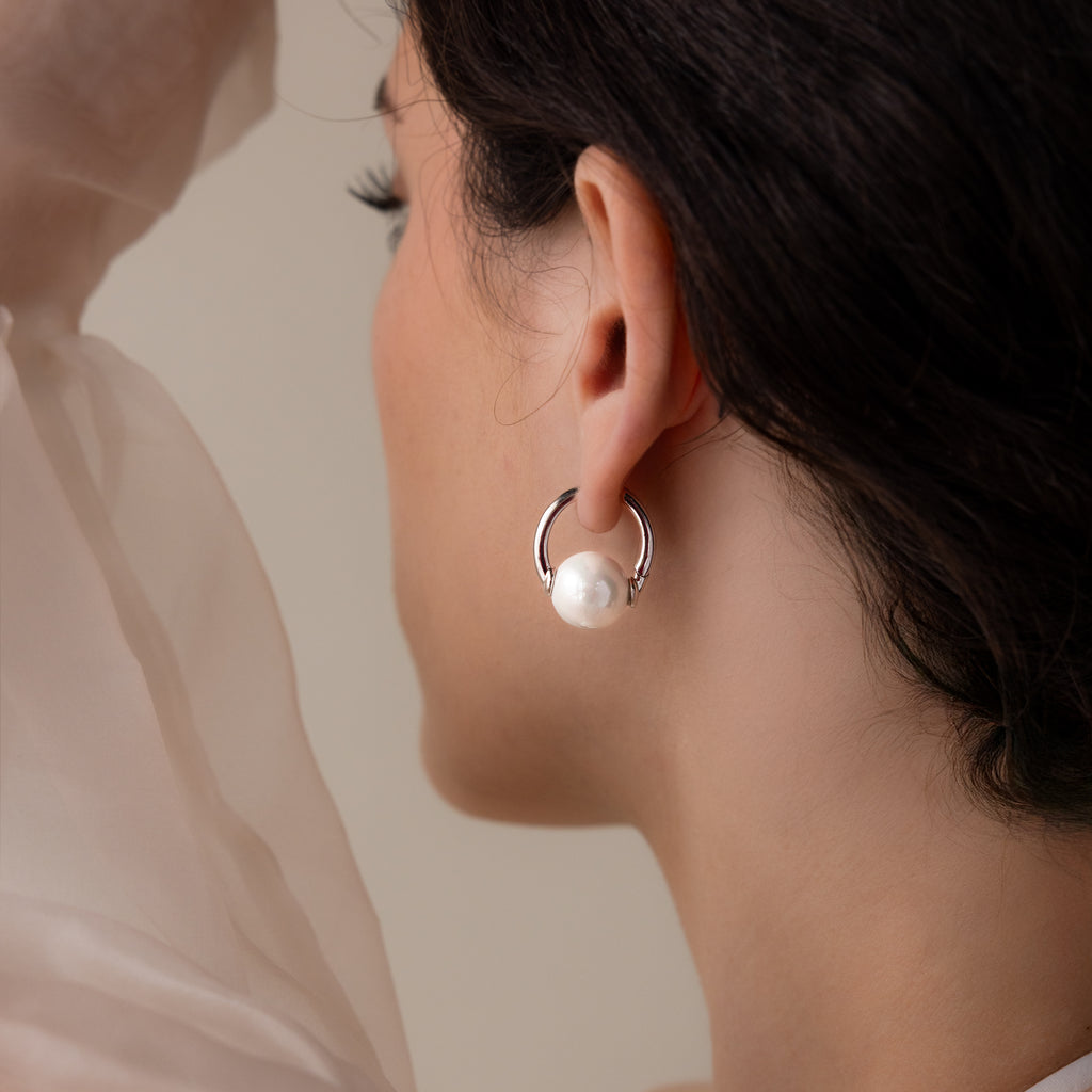 A woman seen from behind wears Bold Round Pearl Hoops featuring a large white pearl—perfect statement earrings for any occasion.