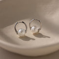 Bold Round Pearl Hoops in Silver feature white pearls on a smooth, beige surface—an ideal choice for modern jewelry lovers.