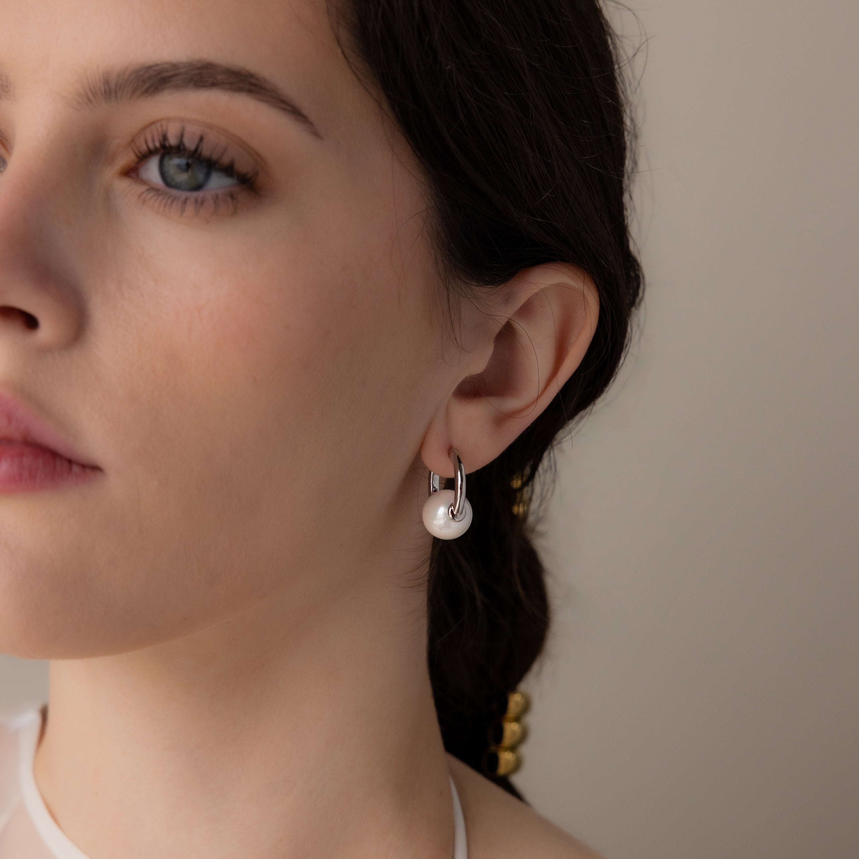 Close-up of a woman wearing Bold Round Pearl Hoops in Silver—modern silver hoop earrings featuring a white pearl, as she looks slightly to the left.
