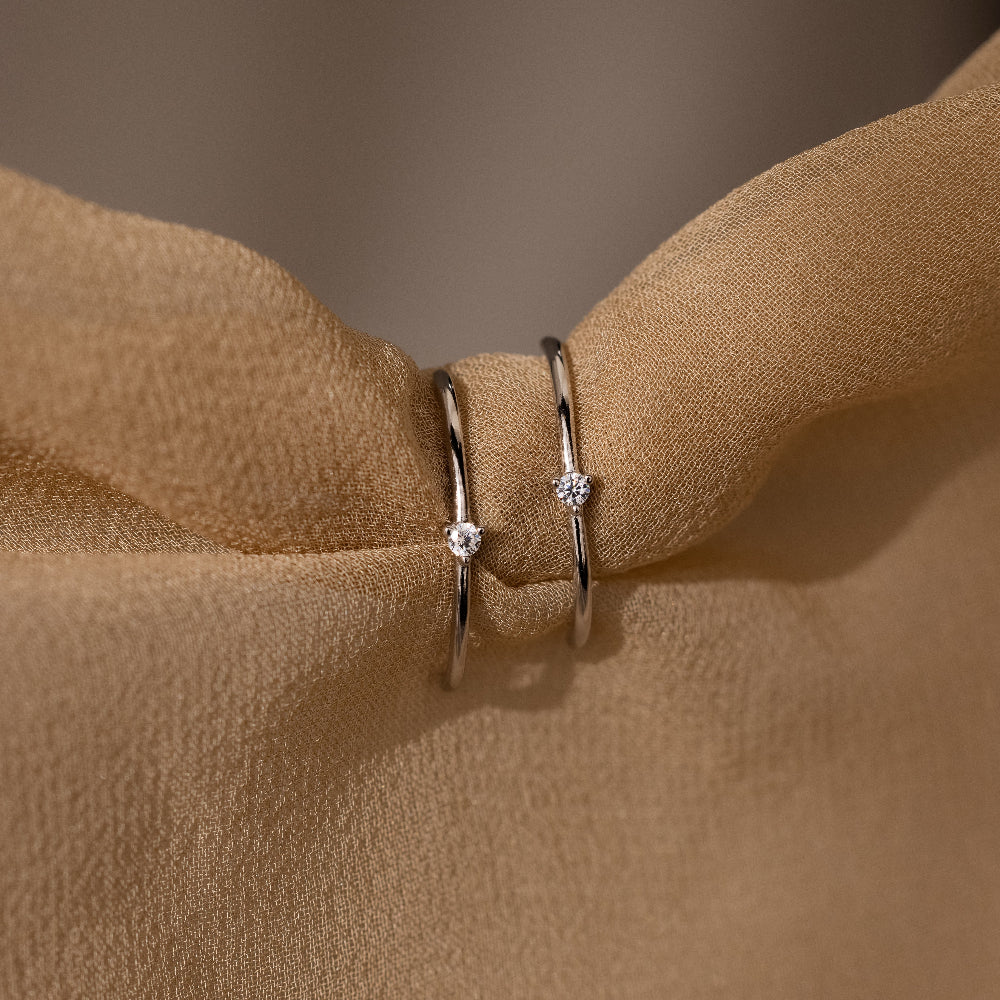 Two silver earrings with small diamonds on a brown fabric background