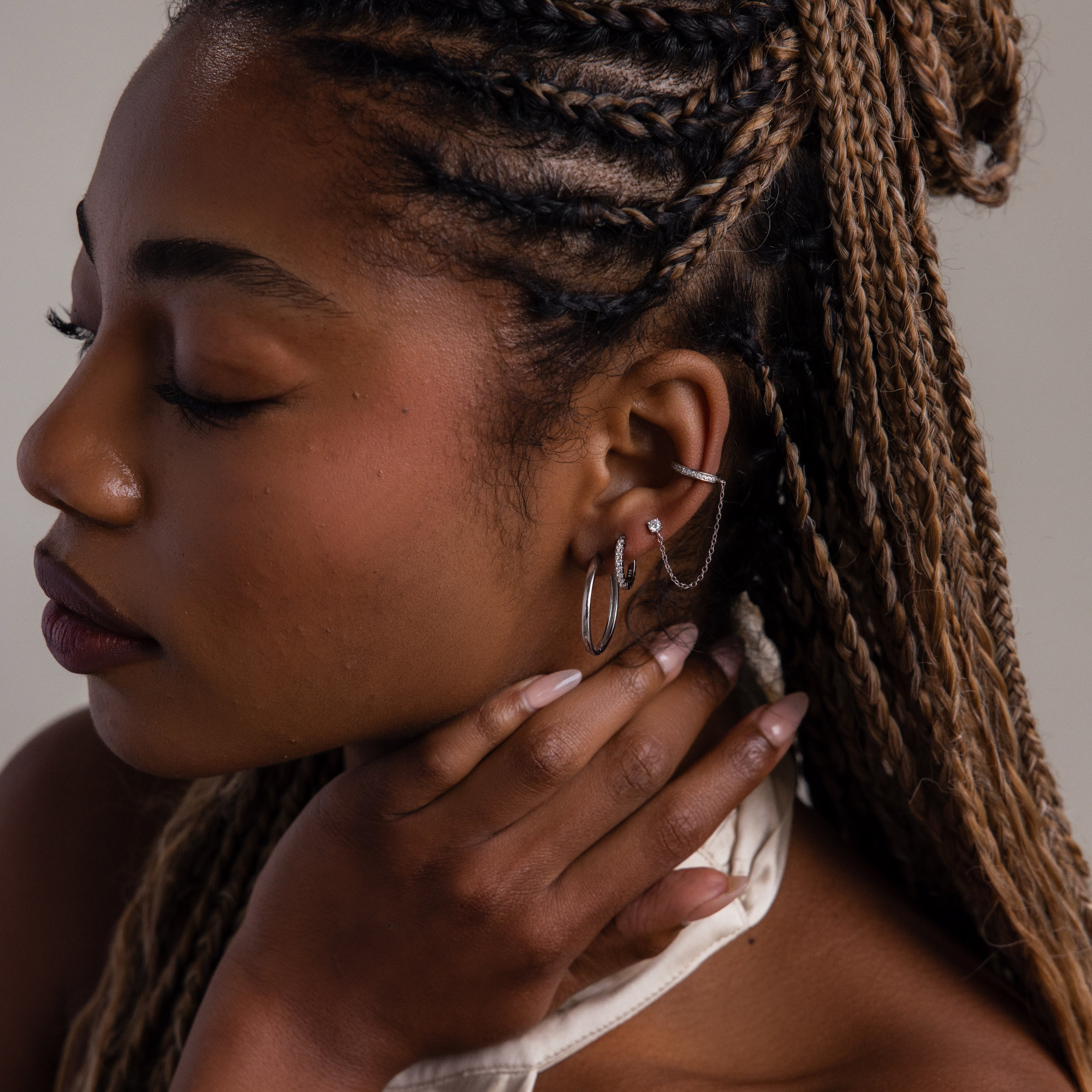 Woman with braided hair wearing various hoop earrings, looking down.